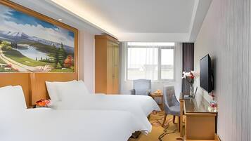 A hotel room with two beds, a desk with a laptop, a TV, and a large window with a mountain landscape view.