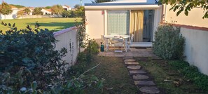 Eine Terrasse mit Tisch und Stühlen, ein kleiner Garten mit trittfesten Steinen und ein Gebäude mit einer Schiebeglastür.