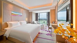 A hotel room with a large bed, a desk, a chair, and a view of the city through large windows. - Lavande Hotel (Ganzhou)