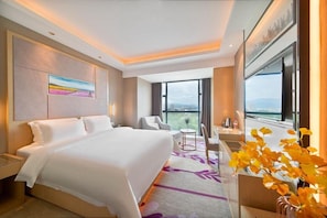 A hotel room with a large bed, a desk, a chair, and a view of the city through large windows. - Lavande Hotel (Ganzhou)