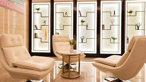 A modern lounge area with three leather chairs, a small round table, and a decorative wall with geometric patterns and small plants. - Lavande Hotel (Ganzhou)