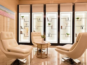A modern lounge area with three leather chairs, a small round table, and a decorative wall with geometric patterns and small plants. - Lavande Hotel (Ganzhou)