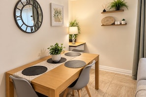 A dining area with a wooden table, grey chairs, a potted plant, and a wall-mounted clock. - Beautiful 3 bed, 2 bath apartment with free on-road parking, WiFi & bills inc. (Parade)