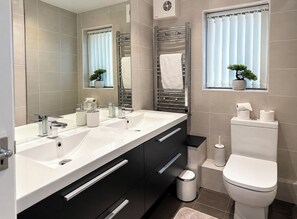A modern bathroom with dual sinks, a toilet, and a window with blinds. - Beautiful 3 bed, 2 bath apartment with free on-road parking, WiFi & bills inc. (Parade)