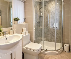 Een moderne badkamer met een douchecabine van glas, een witte wastafel en een toilet.