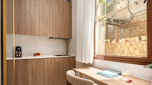 Una cocina compacta con armarios de madera, una encimera blanca, un lavamanos integrado y una ventana con vistas a un muro de piedra y vegetación.