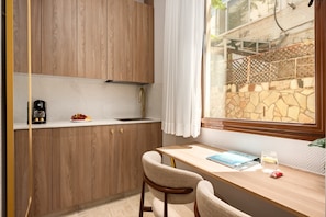 A compact kitchen with wooden cabinets, a white countertop, a built-in sink, and a window with a view of a stone wall and greenery. - Baraca Boutique- Apartments in Jerusalem (Jerusalem)
