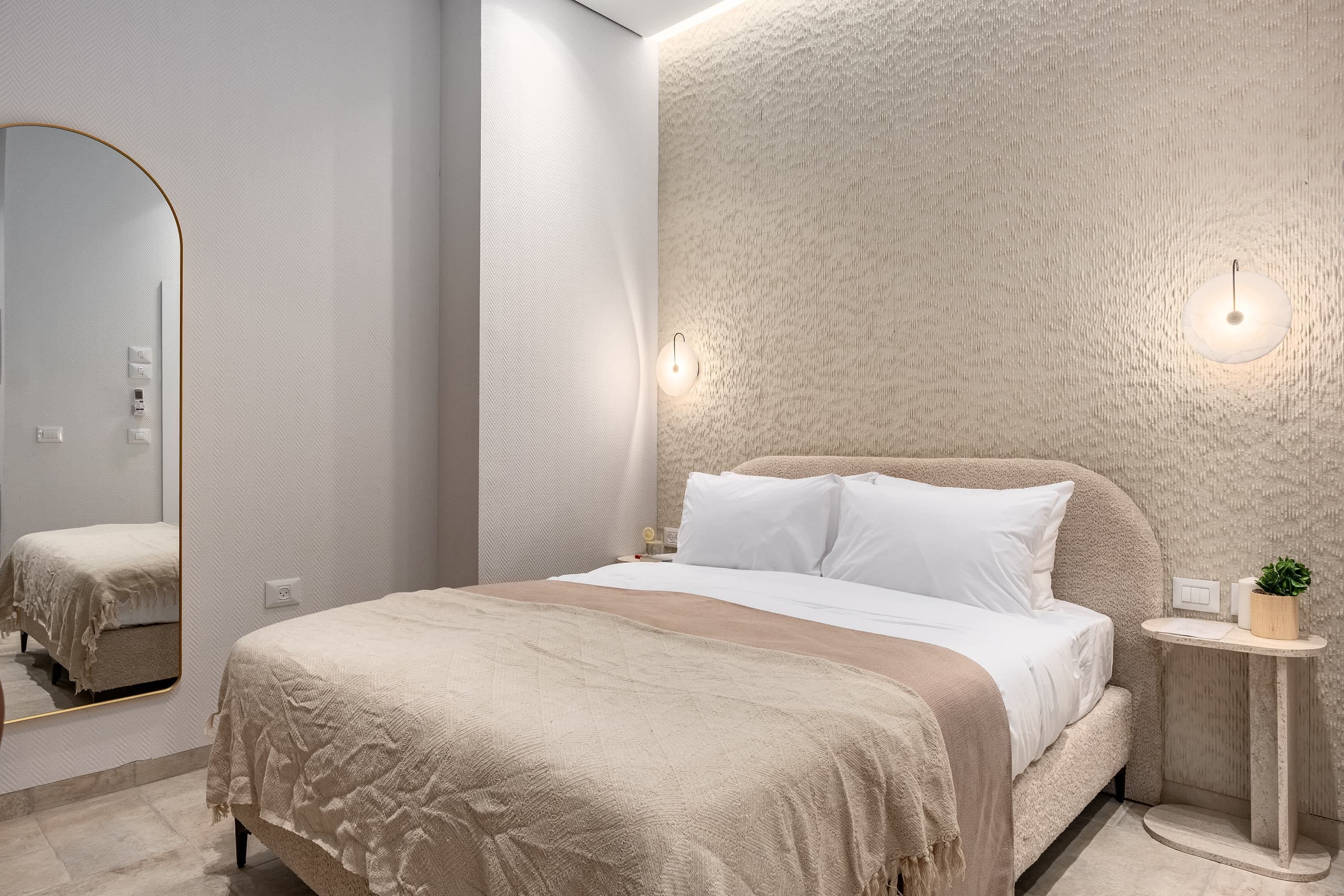 A modern bedroom with a large bed, a mirror, and a textured wall.