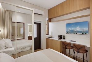 Habitación de hotel con una cama, un escritorio con dos sillas, un ventanal grande y un cuadro en la pared.