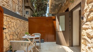 Un pequeño patio exterior con muros de piedra, una puerta de madera y una mesa con sillas.