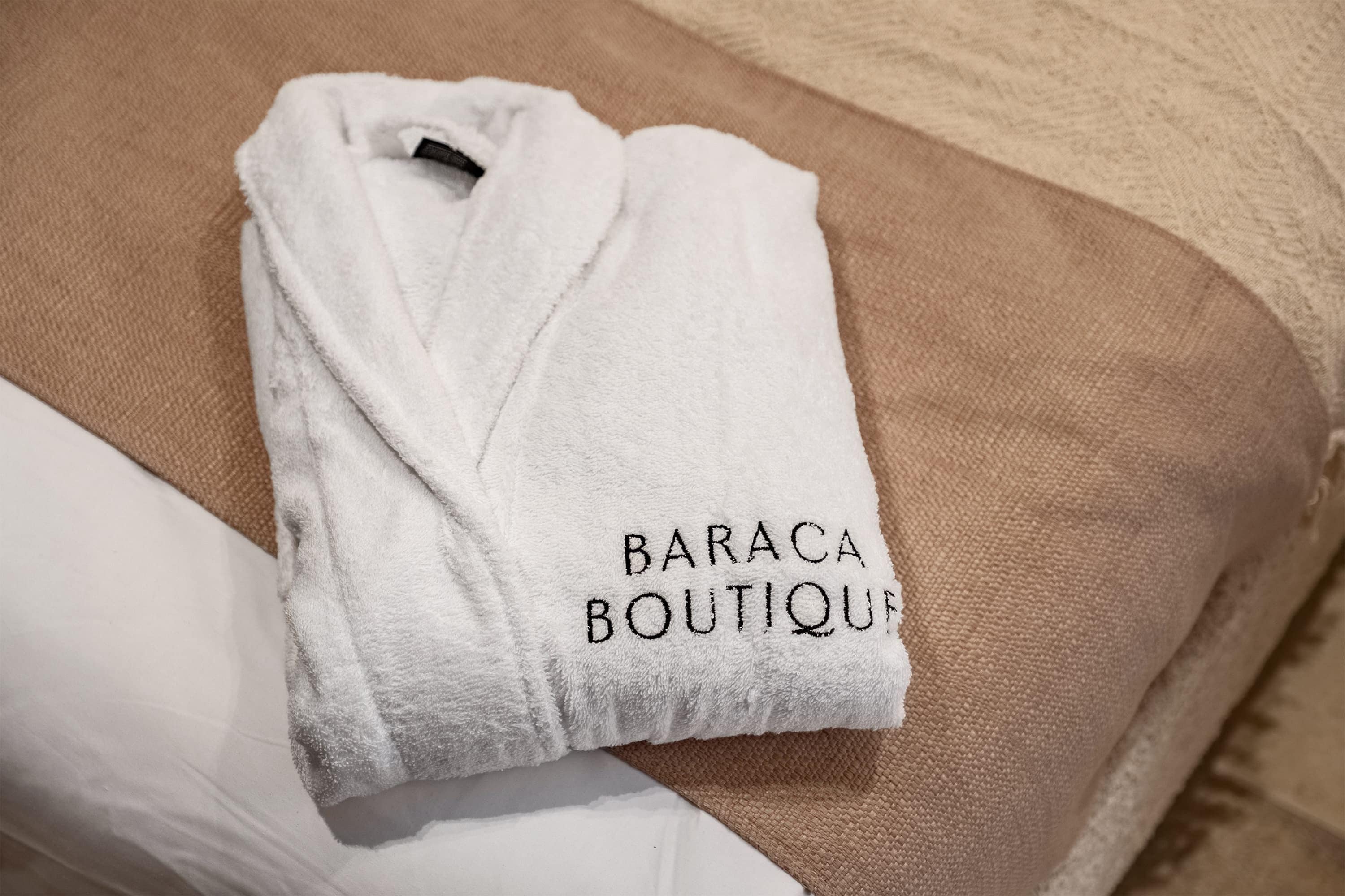 Una toalla blanca con el texto 'BARACA BOUTIQUE' sobre un sofá color beige.
