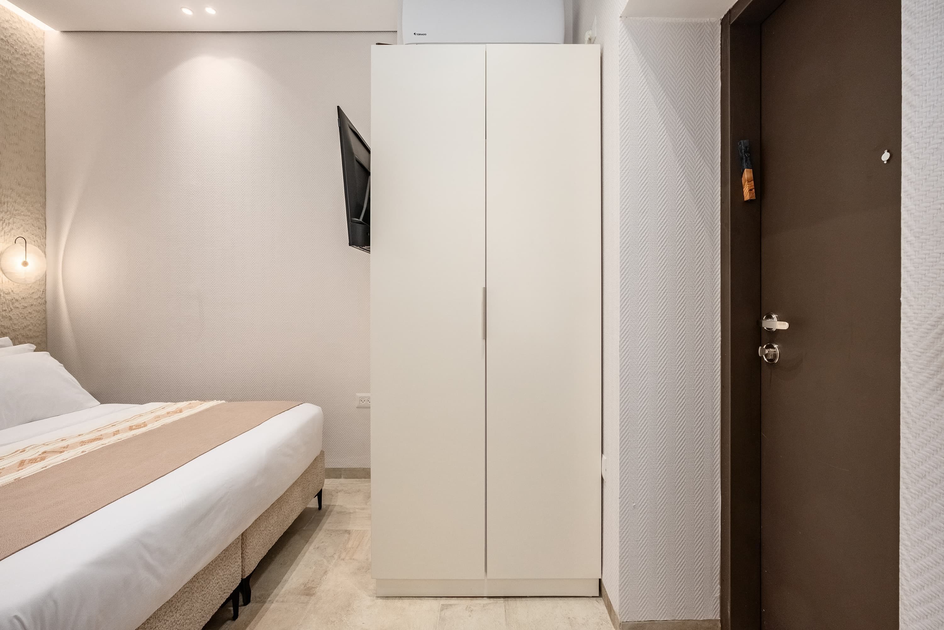 Quarto com cama, guarda-roupa, luz na parede e porta.