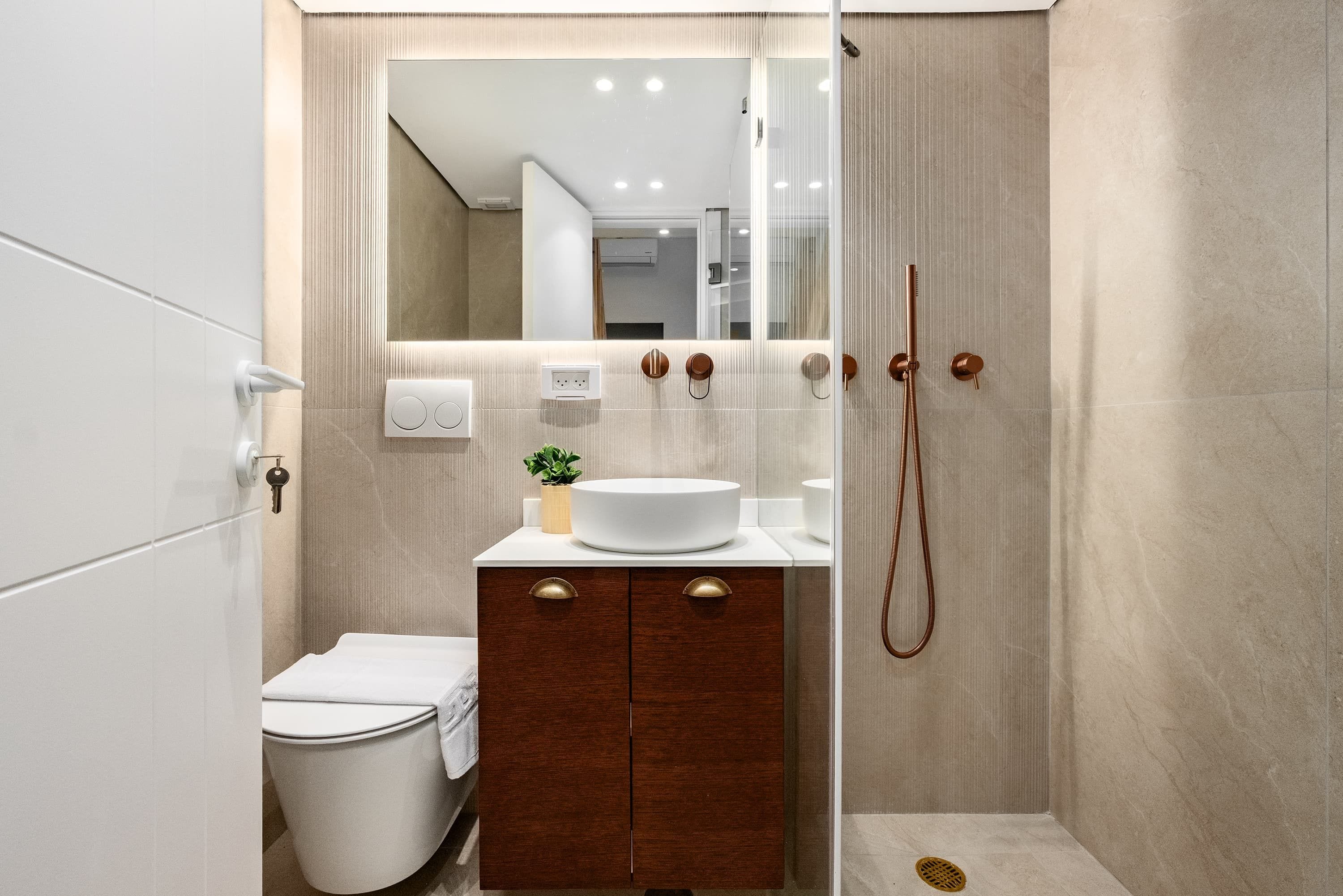 A modern bathroom with a white sink, wooden vanity, and a glass shower enclosure.