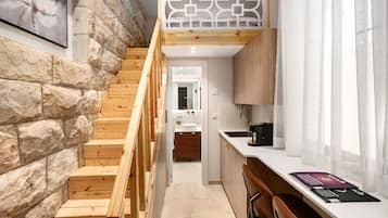 Una escalera conduce a un dormitorio tipo loft con piso de madera, pared de piedra y un panel geométrico blanco.