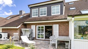 A two-story house with a patio area featuring outdoor furniture and a large window overlooking the garden. - "Ebbe" Holiday Apartment with Private Terrace, Shared Garden, and Wi-Fi (Rodenäs)