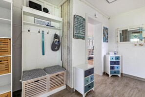A room with a white wardrobe, a bench with storage, a small cabinet with drawers, and a wall with a sign.