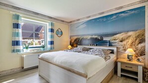 A bedroom with a large bed, a window with curtains, a wall-mounted clock, and a beach-themed mural. - "Ebbe" Holiday Apartment with Private Terrace, Shared Garden, and Wi-Fi (Rodenäs)