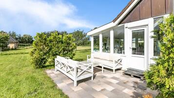 A covered outdoor seating area with a bench and table, surrounded by a well-maintained lawn and trees.