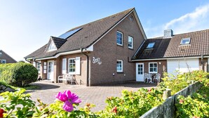 A two-story brick house with a sloped roof, a front porch with a bench, and a small garden area with flowers and shrubs. - "Ebbe" Holiday Apartment with Private Terrace, Shared Garden, and Wi-Fi (Rodenäs)