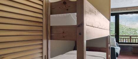 A bunk bed with a wooden headboard in a room with a view of greenery outside.