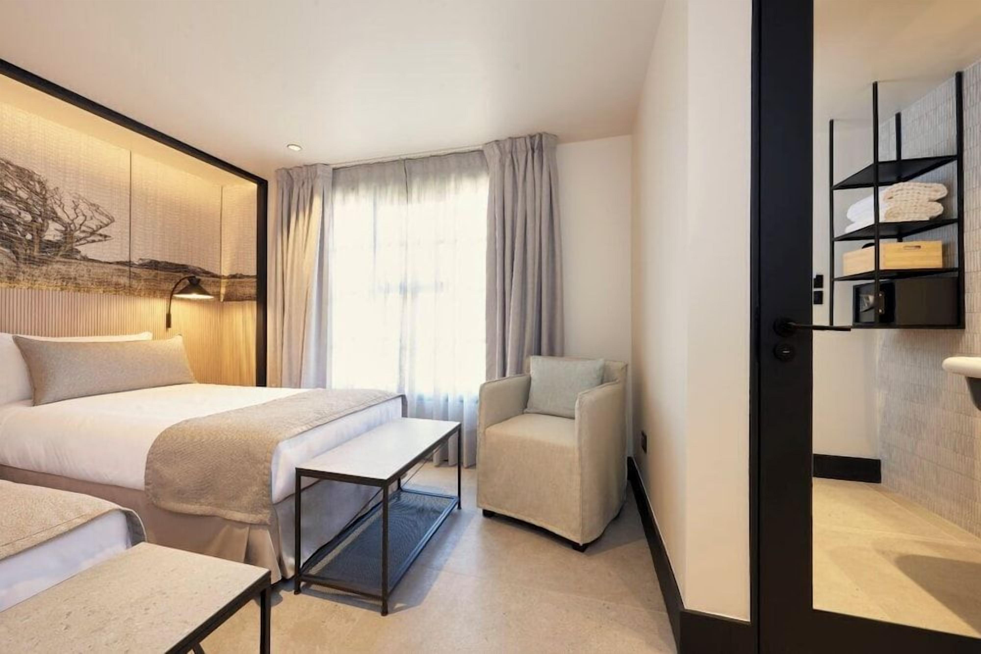 Habitación de hotel con una cama, una silla, un escritorio y una repisa en la pared con toallas.