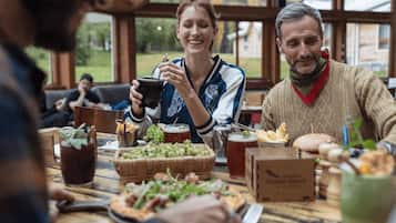 Un grupo de personas sentadas en una mesa de madera con comida y bebidas, en una habitación con ventanas amplias y vistas a la vegetación.