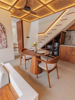 A modern interior with a wooden dining table, chairs, and a kitchen area with a staircase. - NEW 1BR Villa Svargi 1 Surf and Sanctuary Private pool (Pecatu, South Kuta, Badung Regency, Bali 80361)