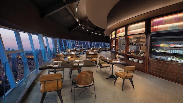 A modern restaurant with high tables and chairs, a dessert display, and a city view. - Yudu Hotel (Chongqing)