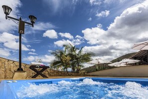 A swimming pool with a stone wall, palm trees, and umbrellas. - Hospederia y Centro de Convenciones Duruelo (Villa de Leyva)