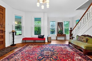 Une pièce spacieuse avec un grand tapis décoratif, un banc, un canapé et un escalier.