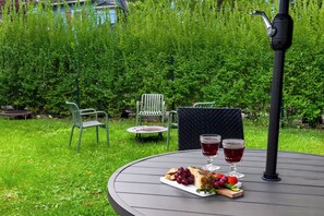 Une table ronde avec une assiette de nourriture, deux verres d’une boisson rouge et un plateau de fromages.