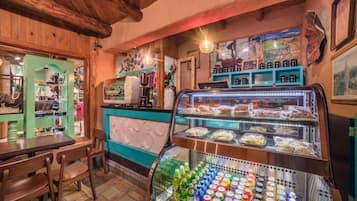 Una cafetería con mostrador, zona de estar y vitrina con comida y bebidas.