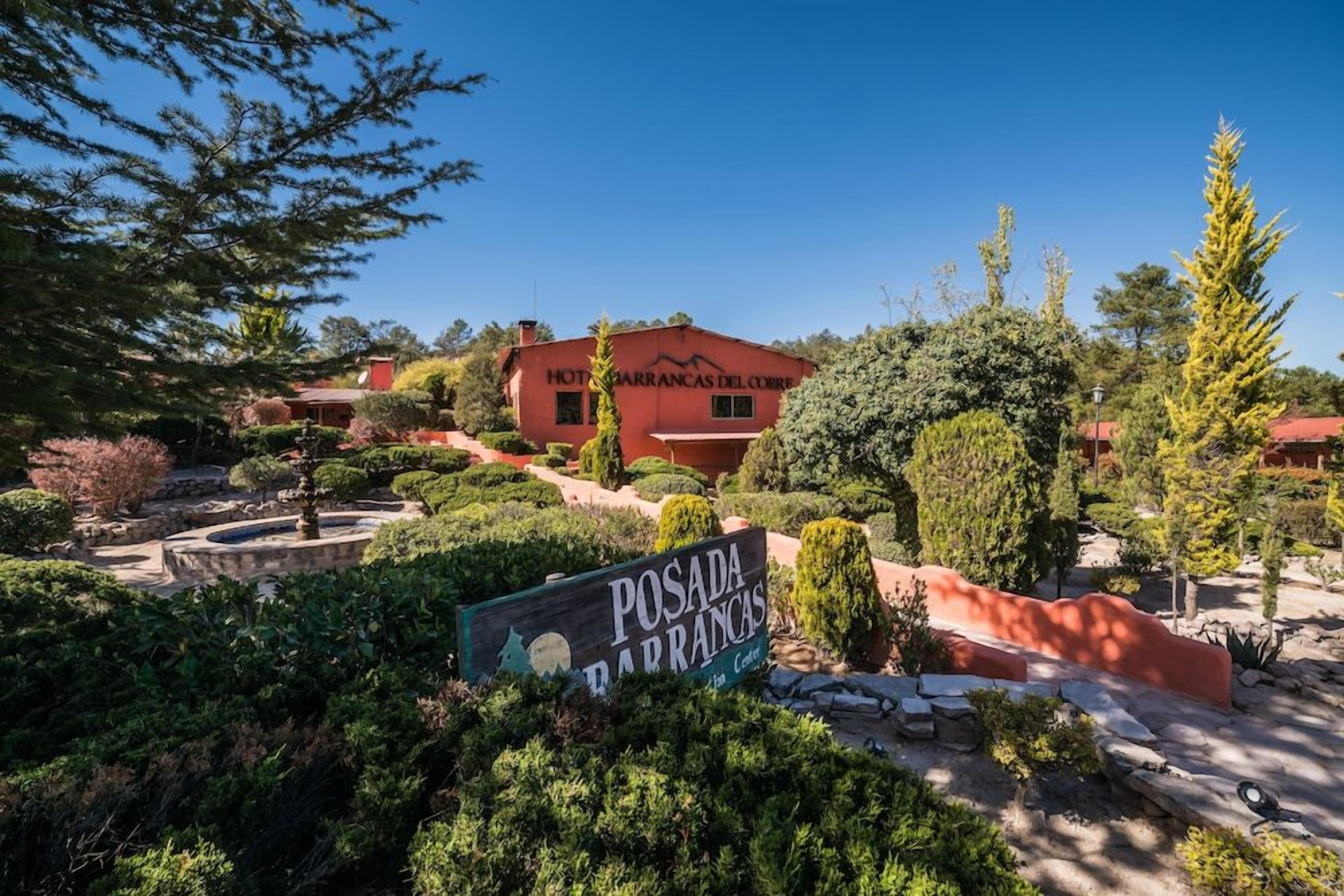 A hotel named 'Posada Barrancas del Corbe' with a sign in front, surrounded by landscaped gardens and trees.