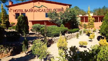 Un hotel llamado 'Hotel Barrancas del Cobre' con fachada roja, rodeado de jardines y árboles diseñados.