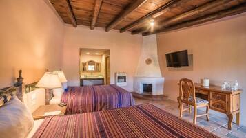 Un dormitorio con techo de madera, una cama con ropa de cama a rayas, un escritorio con silla, un televisor y una chimenea.