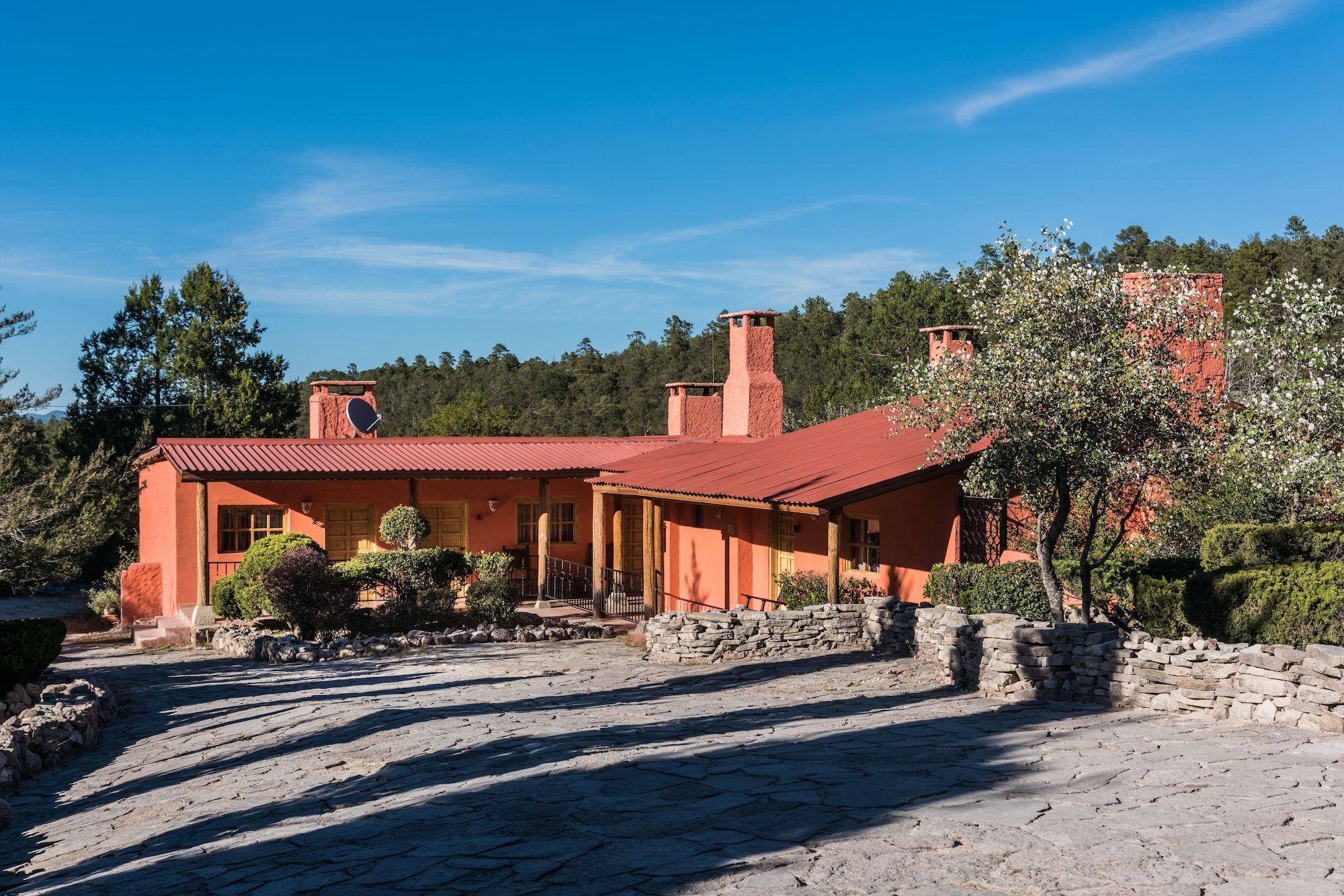 A rustic house with a red roof, stone walls, and a paved driveway.