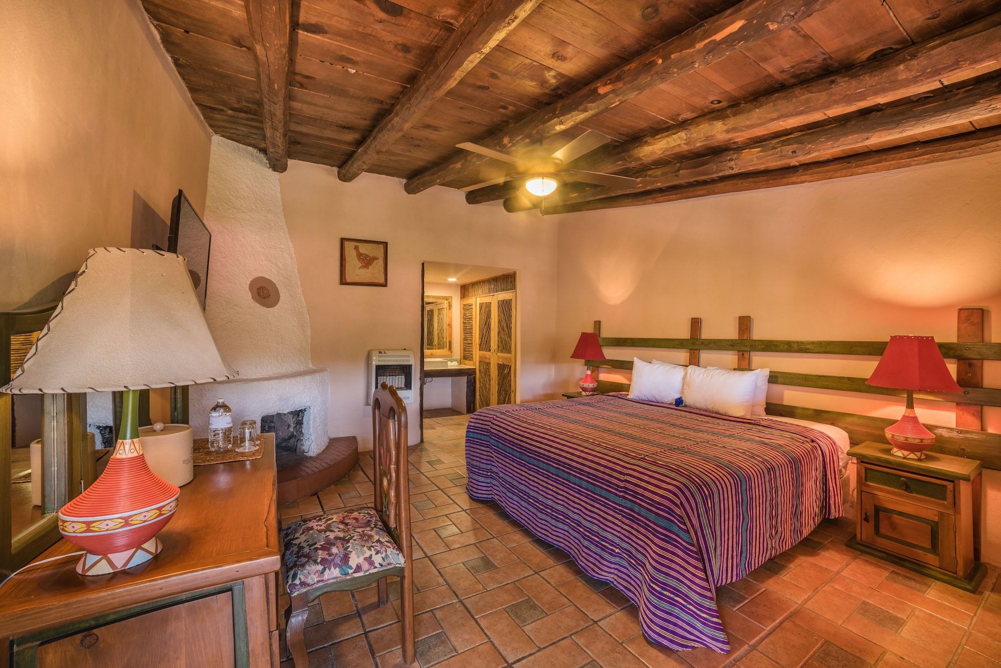 A cozy bedroom with a wooden ceiling, a bed with a striped bedspread, a chair, a nightstand, and a lamp.