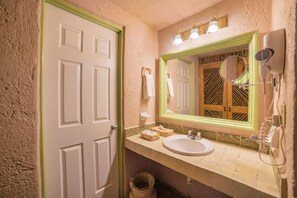 A bathroom with a white door, a sink, a mirror, and a hairdryer mounted on the wall. - Hotel Barrancas del Cobre (Urique)
