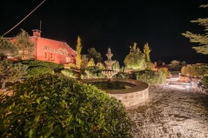 Ein Hotel mit einem Brunnen, gepflegten Gärten und einem klaren Nachthimmel.