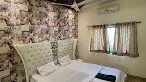 A bedroom with a large bed, a ceiling fan, and a patterned wallpaper. - 23 West, Malavli (Pune)
