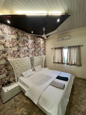 A bedroom with a large bed, a ceiling fan, and a patterned wallpaper. - 23 West, Malavli (Pune)