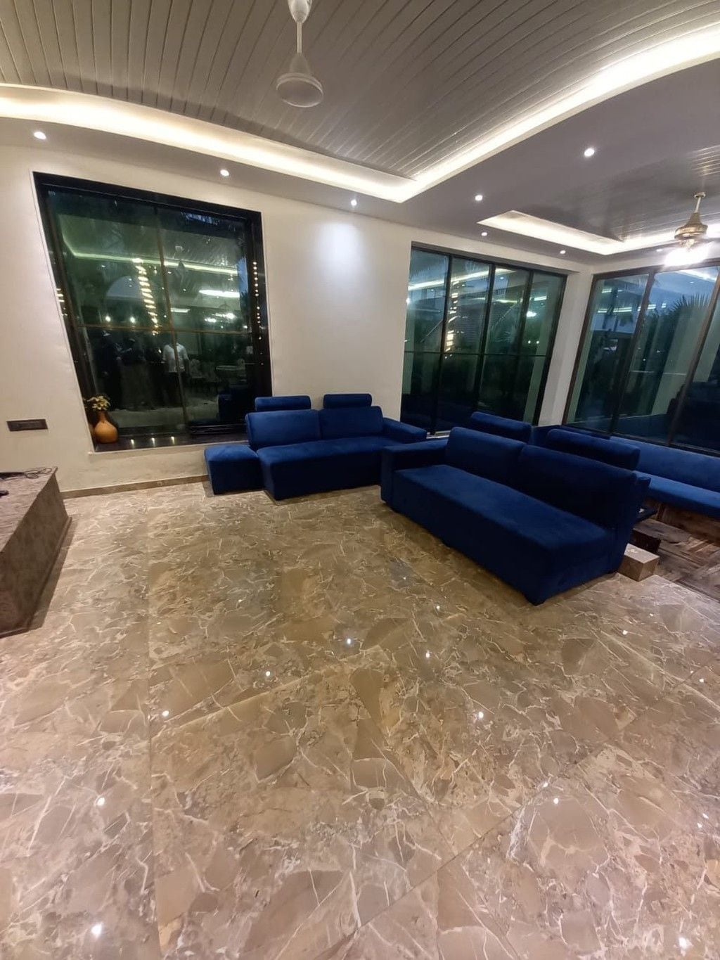 Una sala de estar moderna con piso de mármol, sofás azules y ventanas amplias.