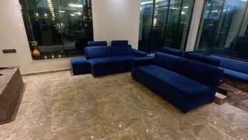 Una sala de estar moderna con piso de mármol, sofás azules y ventanas amplias.