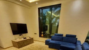 A modern living room with a flat-screen TV, a marble floor, and a large window with a view of palm trees. - 23 West, Malavli (Pune)