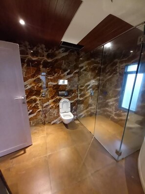 A modern bathroom with a marble wall, a toilet, and a glass shower enclosure. - 23 West, Malavli (Pune)