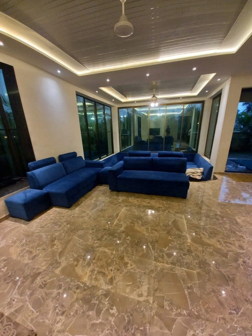 A modern living room with a sectional sofa, large windows, and a marble floor.