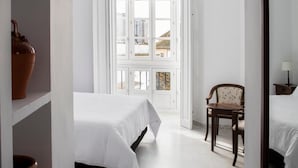 A hotel room with a bed, a chair, a window with a view, and a shelf with a vase.