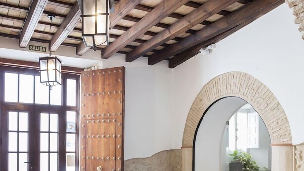 A rustic interior with a stone floor, wooden door, and arched window.