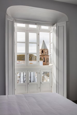 A bedroom with a large bay window, a bed, and a view of a historic building. - Medina Sidonia (Medina-Sidonia)