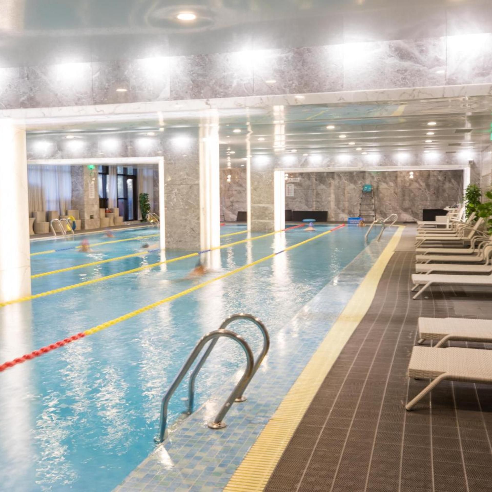 An indoor swimming pool with lanes, a diving board, and lounge chairs.